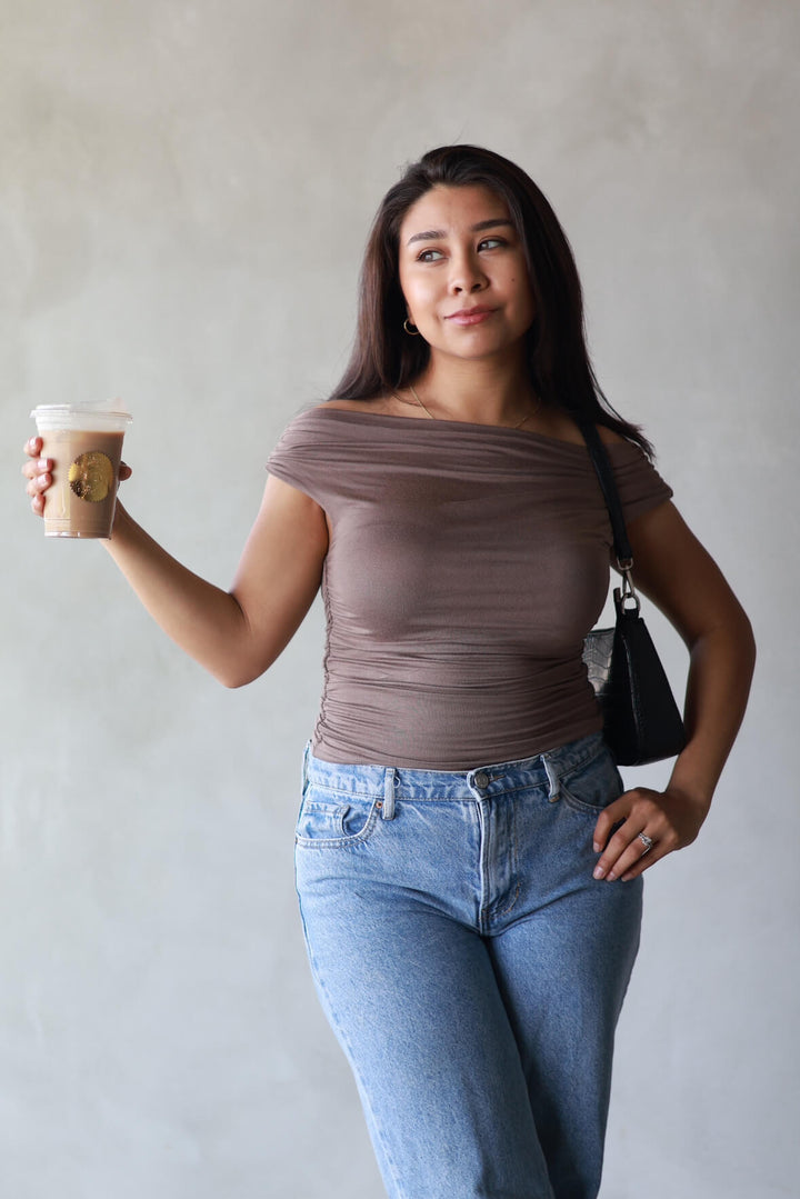 girl wearing a brown top paired with jeans and enjoying a iced latte