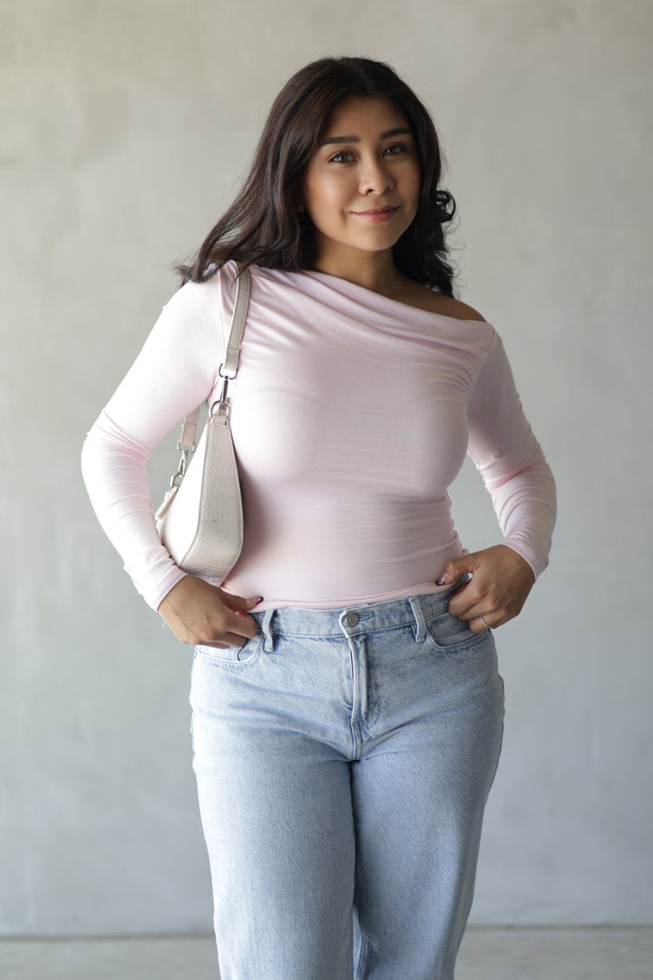 baby pink off the shoulder top paired with light wash jeans and cream bag 