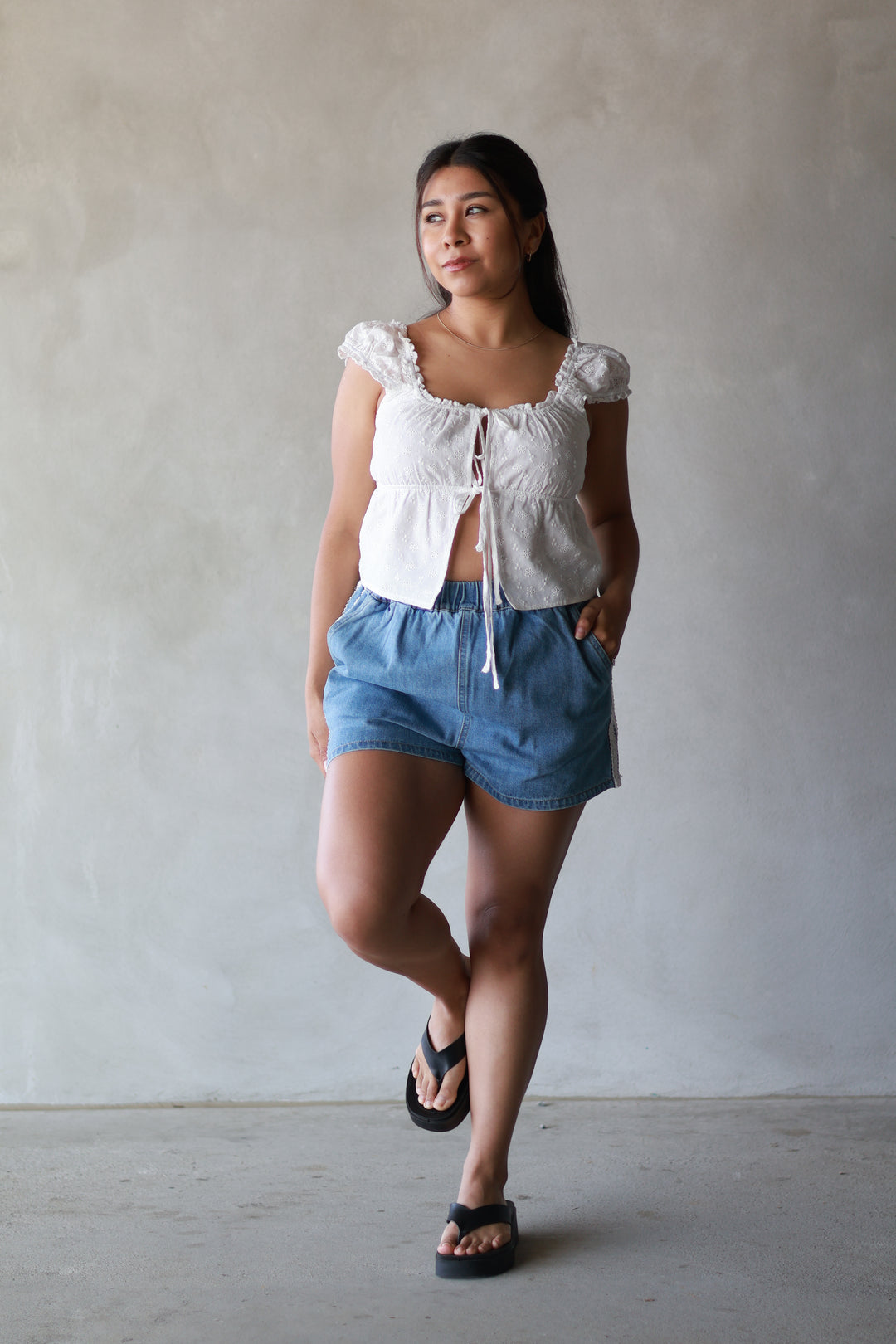 women wearing a white top with denim shorts and black flip flops