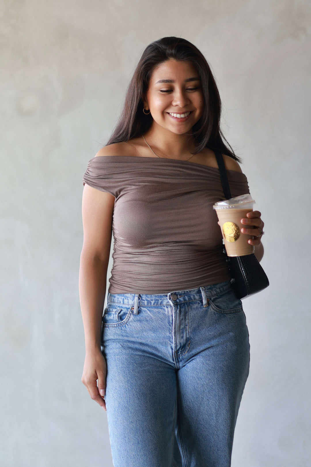 girl wearing a brown top paired with jeans and enjoying a iced latte