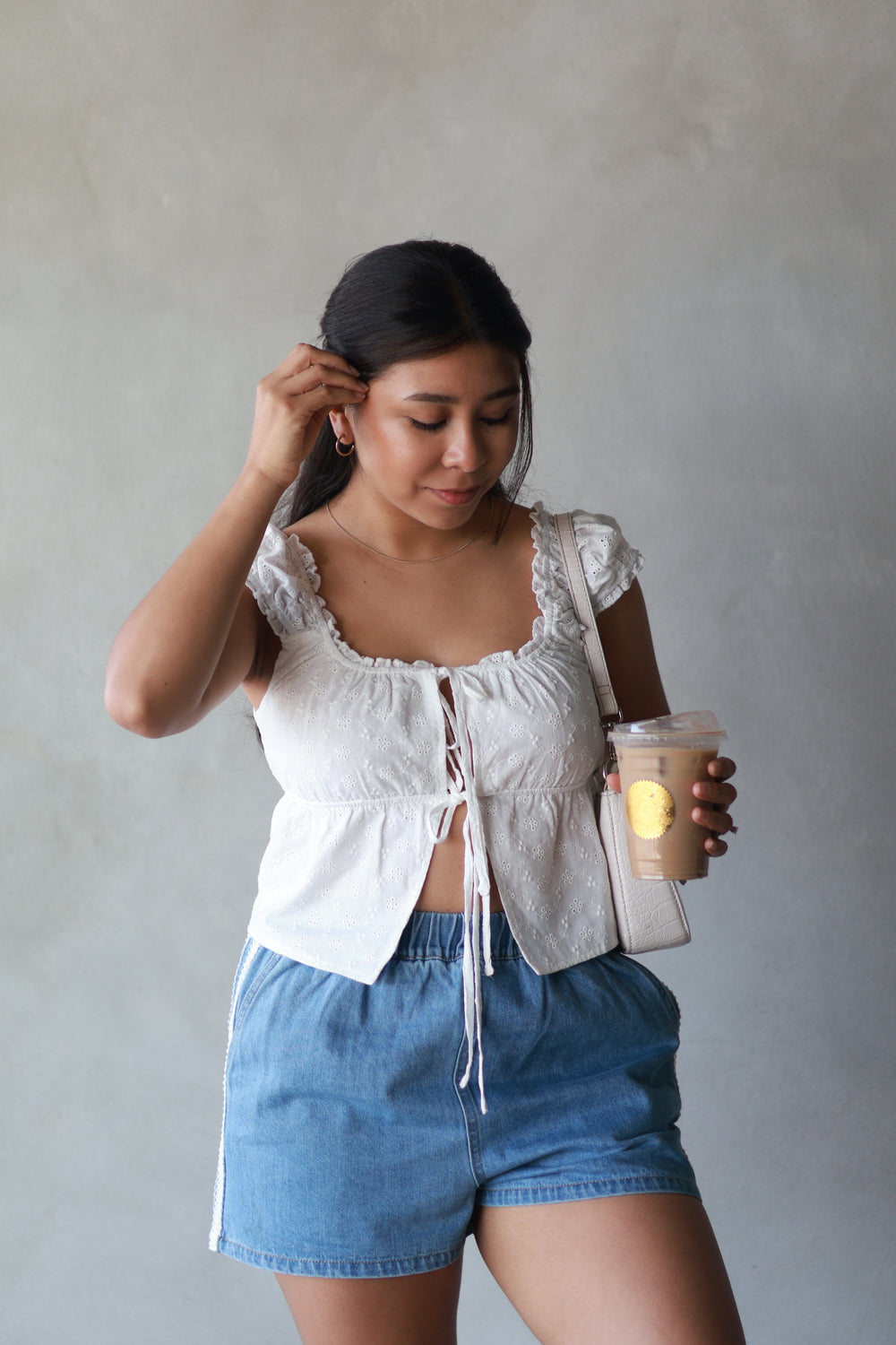 girl wearing a white top paired with lace  trim shorts and coffee in her hand