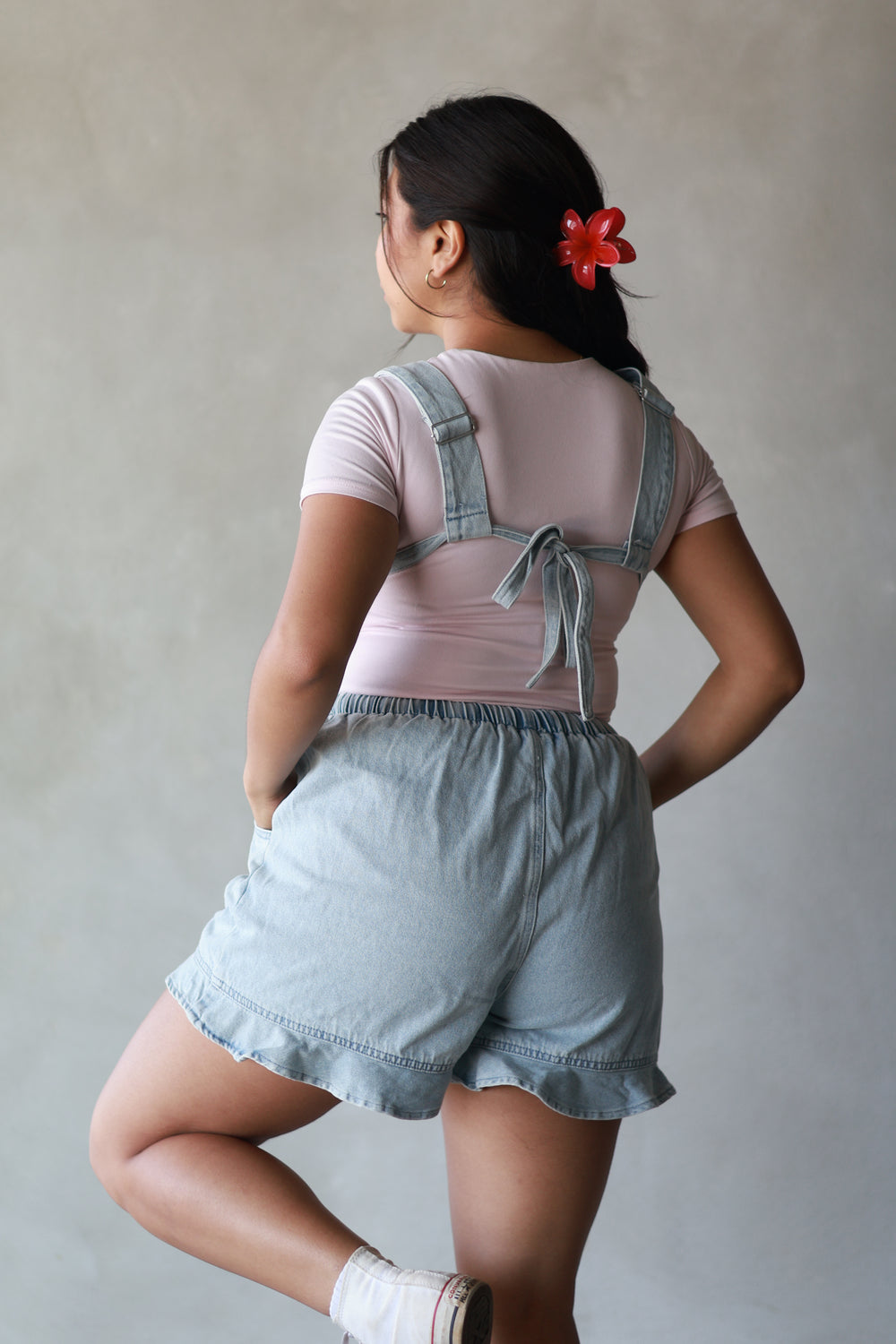 girl showing the back of a pink top paired with light wash overalls