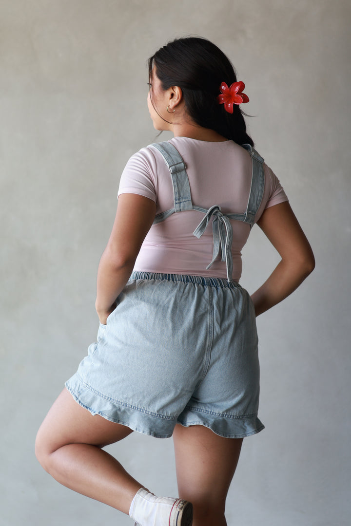girl showing the back of a pink top paired with light wash overalls