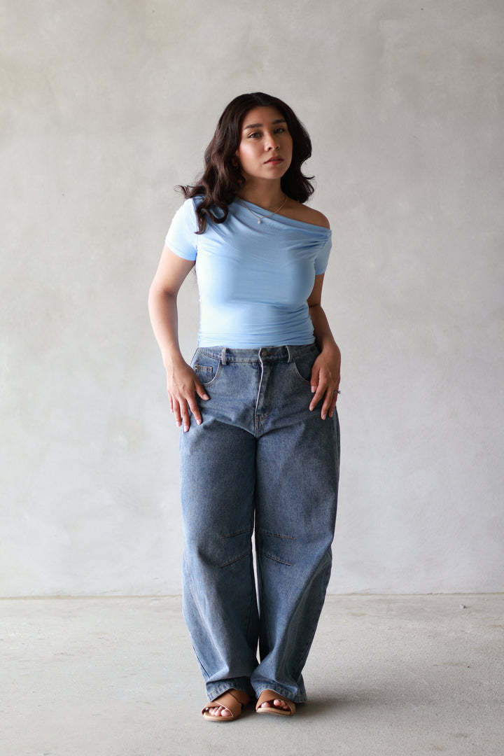women wearing a blue off the shoulder short sleeve top, paired it with barrel jeans, and brown flip flops
