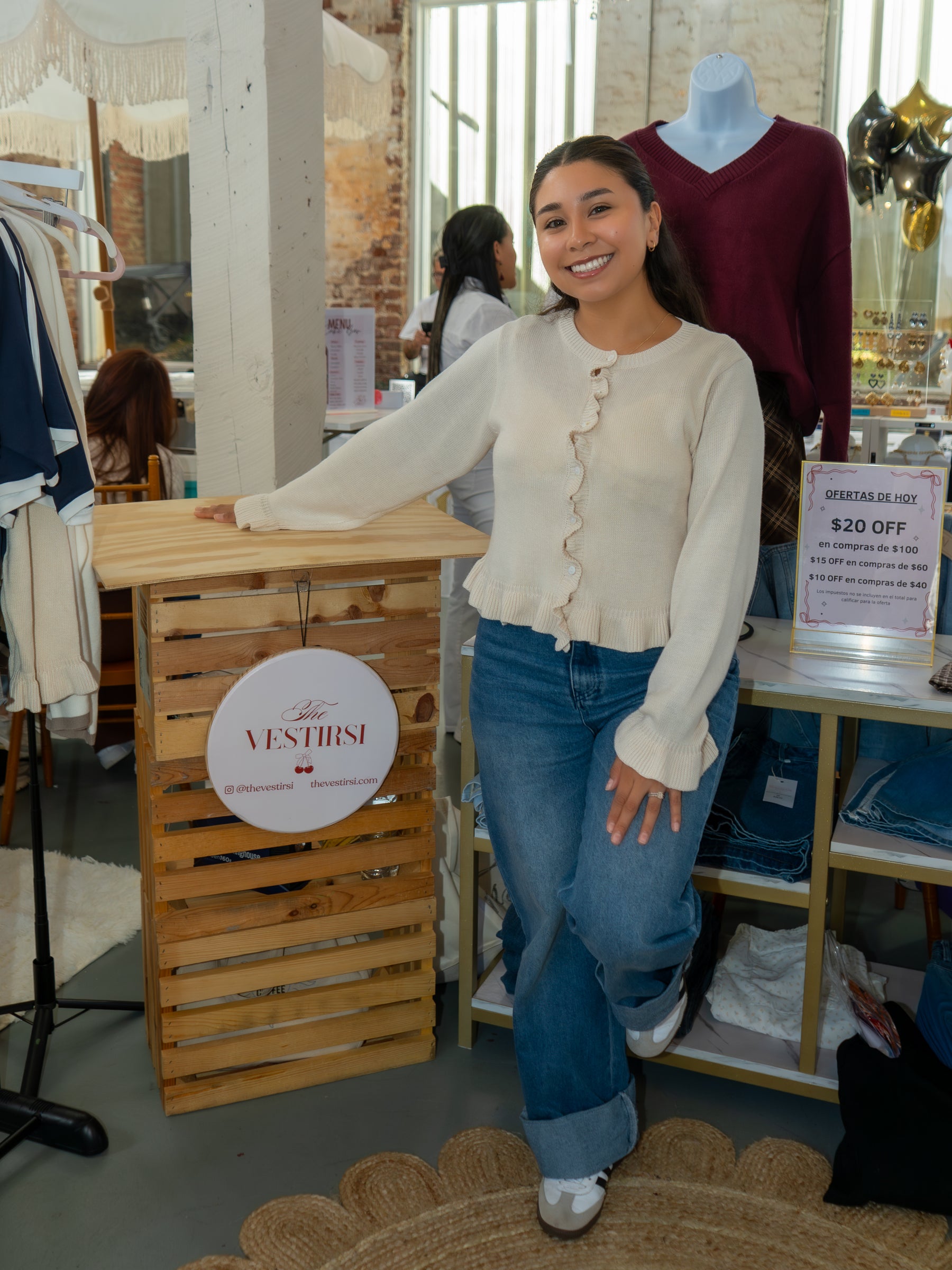 Woman standing next to a wooden display with 'The vestirsi' branding in a store setting.