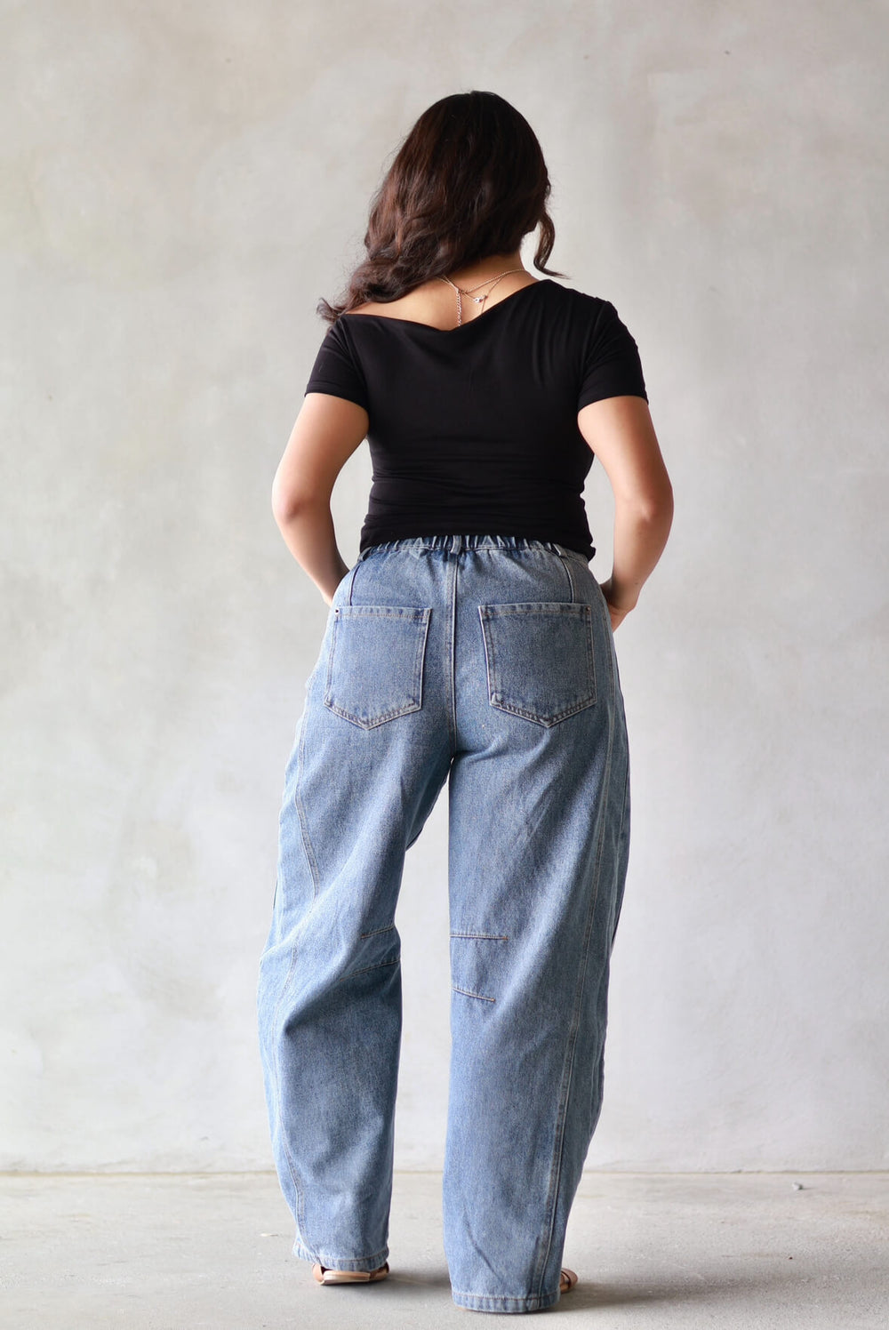 back of a womens trendy outfit with a black top and barrel jeans