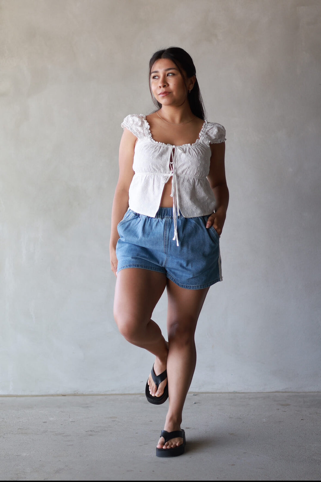 women wearing a white top with denim shorts and black flip flops front view